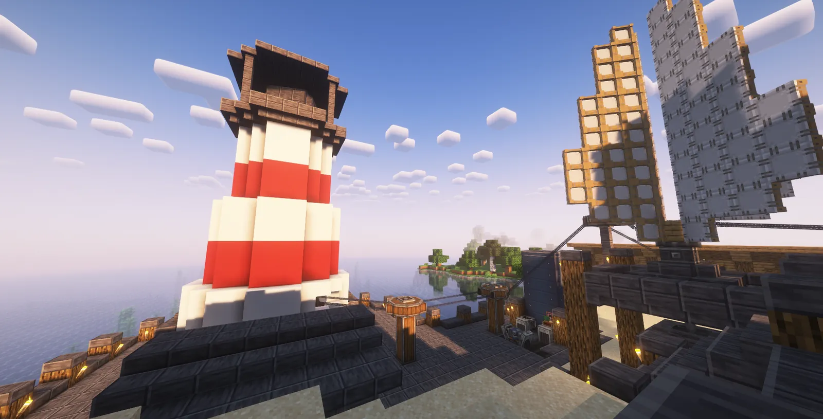 A red and white lighthouse on a harbour pier next to a ship with sails